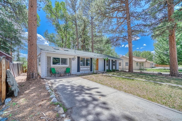 single story home featuring stone siding, fence, and a front lawn