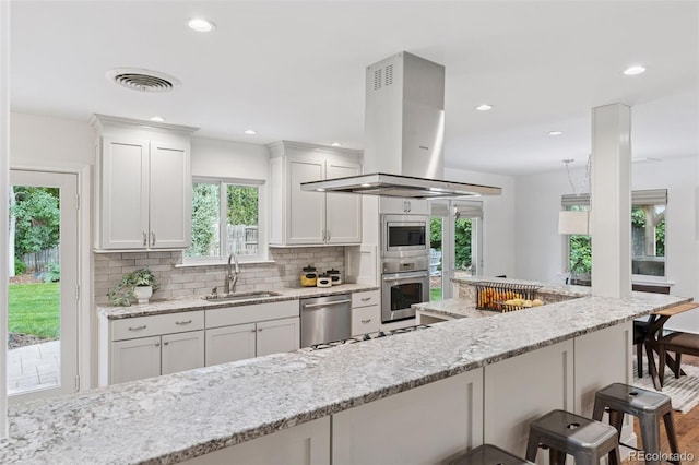 3190 S Detroit St, Denver, CO 80210 - kitchen with island exhaust hood, stainless steel appliances, a kitchen bar, tasteful backsplash, and white cabinets