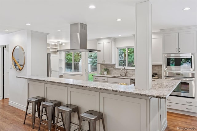 3190 S Detroit St, Denver, CO 80210 - kitchen with stainless steel appliances, island exhaust hood, decorative backsplash, a kitchen bar, and recessed lighting