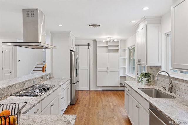 3190 S Detroit St, Denver, CO 80210 - kitchen with island range hood, stainless steel appliances, a barn door, white cabinetry, and light stone countertops
