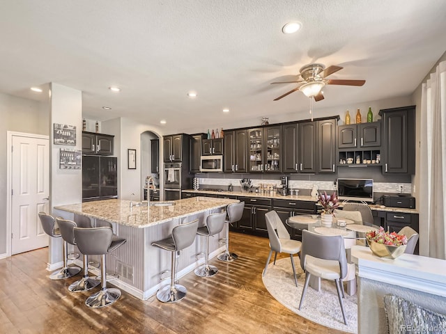 kitchen featuring stainless steel appliances, arched walkways, dark wood-style floors, and a kitchen bar