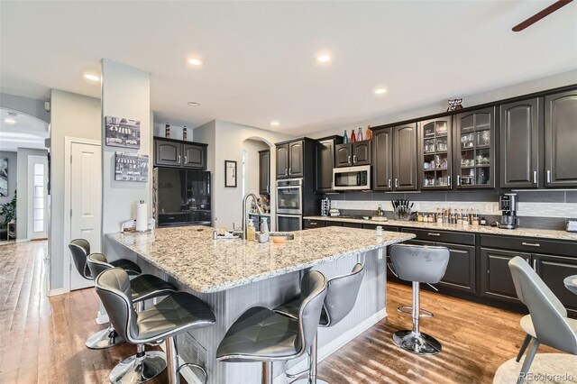 kitchen featuring a breakfast bar, decorative backsplash, appliances with stainless steel finishes, arched walkways, and a sink