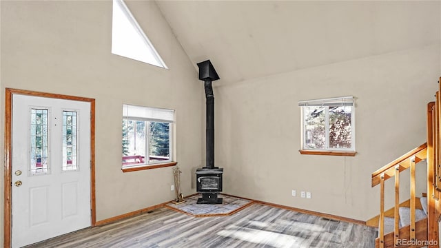 foyer featuring wood-type flooring, high vaulted ceiling, a wood stove, and a wealth of natural light