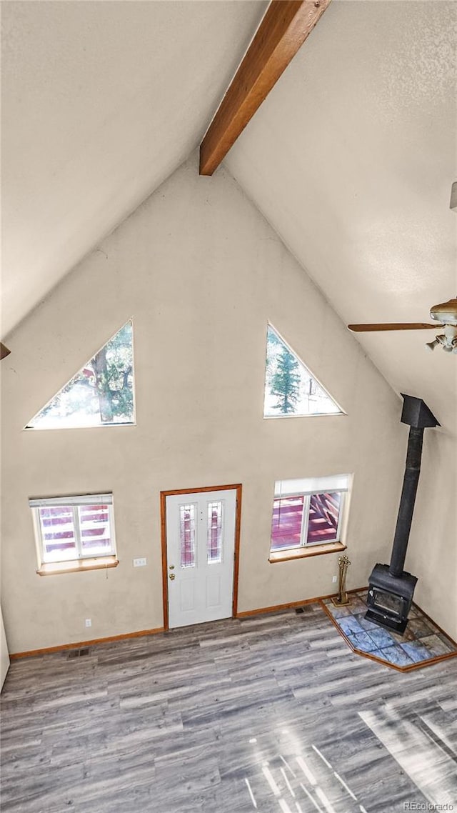 unfurnished living room featuring high vaulted ceiling, light hardwood / wood-style floors, a wood stove, and plenty of natural light