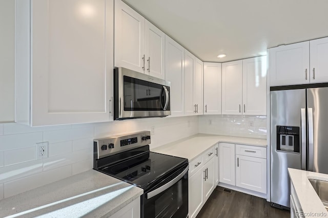 kitchen with appliances with stainless steel finishes, dark hardwood / wood-style flooring, white cabinets, light stone countertops, and decorative backsplash