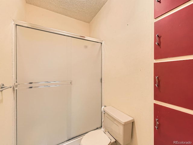 bathroom featuring a shower with door, a textured ceiling, and toilet