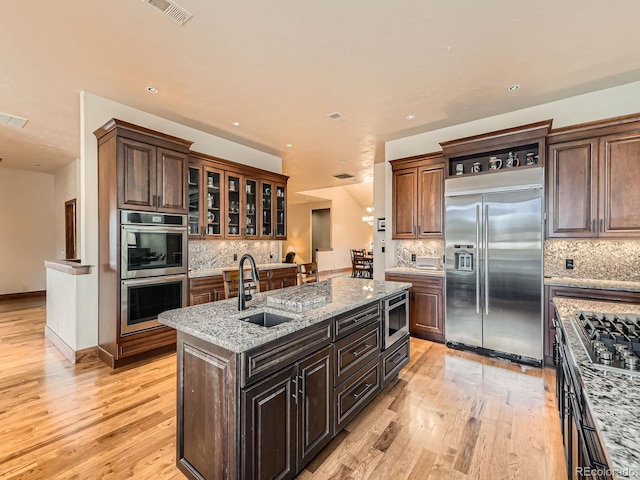 kitchen with light wood finished floors, a sink, backsplash, and appliances with stainless steel finishes