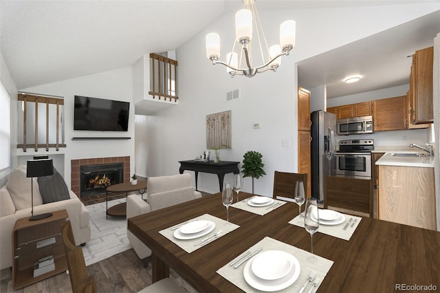 dining room featuring visible vents, a tiled fireplace, wood finished floors, an inviting chandelier, and vaulted ceiling