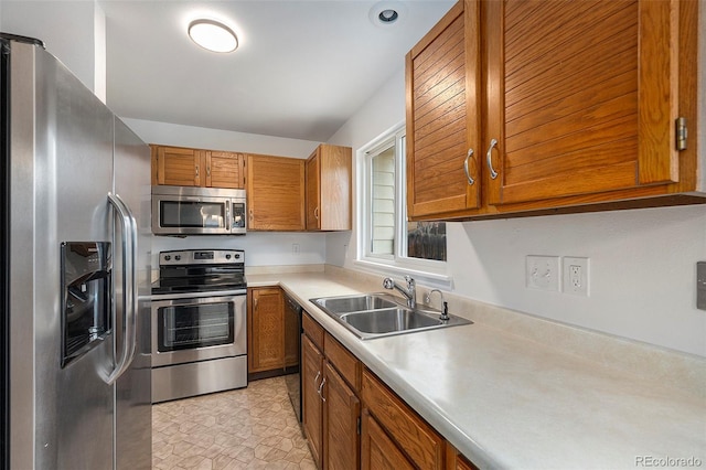 kitchen with brown cabinetry, stainless steel appliances, a sink, and light countertops