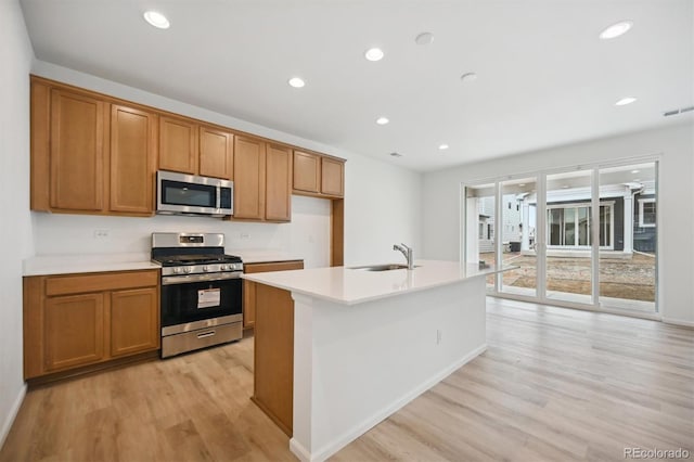 kitchen with appliances with stainless steel finishes, sink, light hardwood / wood-style floors, and an island with sink