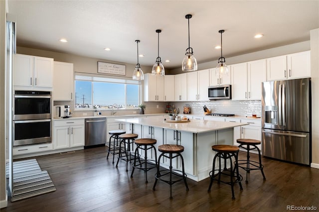 kitchen featuring white cabinets, a center island, decorative light fixtures, stainless steel appliances, and a breakfast bar