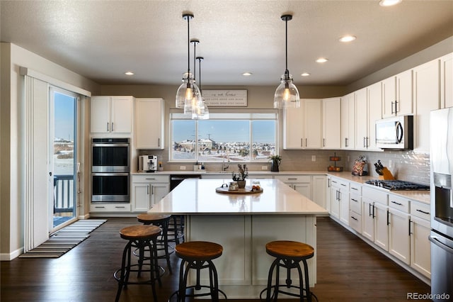 kitchen with appliances with stainless steel finishes, dark wood-type flooring, pendant lighting, white cabinets, and a center island