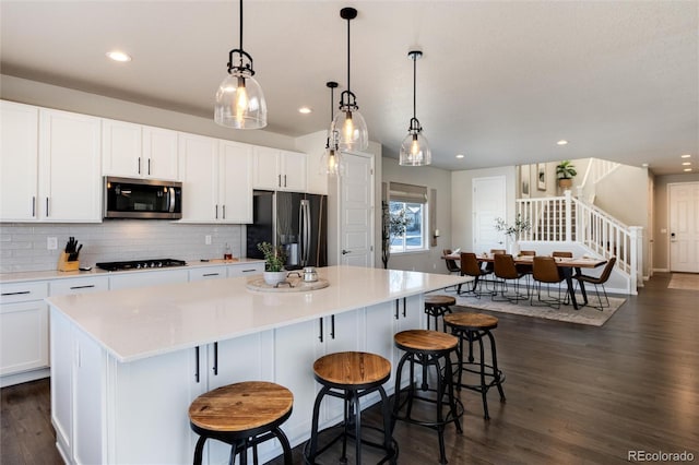 kitchen with white cabinetry, stainless steel appliances, backsplash, a spacious island, and hanging light fixtures