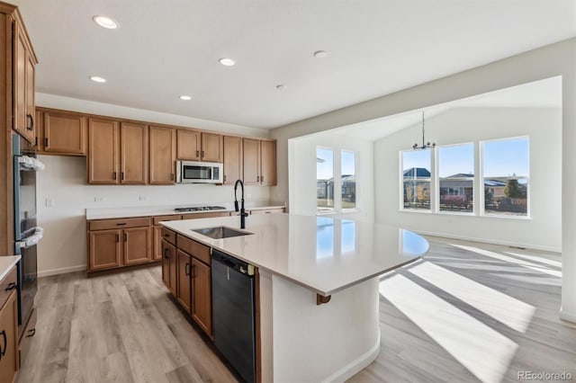 kitchen with lofted ceiling, a kitchen island with sink, sink, light wood-type flooring, and appliances with stainless steel finishes