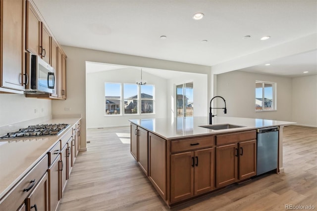 kitchen with sink, pendant lighting, a center island with sink, appliances with stainless steel finishes, and light wood-type flooring