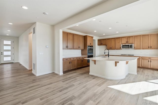 kitchen featuring appliances with stainless steel finishes, light hardwood / wood-style floors, and an island with sink