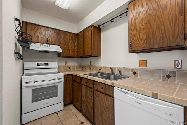 kitchen with white appliances, under cabinet range hood, a sink, light tile patterned floors, and tile countertops