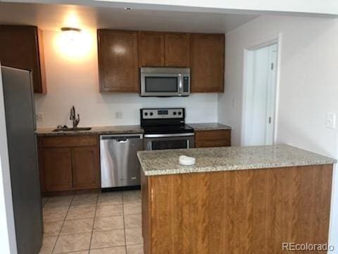 kitchen with light stone countertops, light tile patterned floors, appliances with stainless steel finishes, and sink