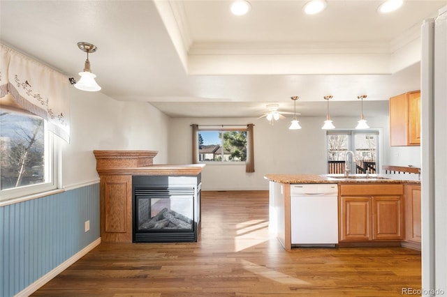 kitchen with white dishwasher, a peninsula, a sink, wainscoting, and light wood-type flooring