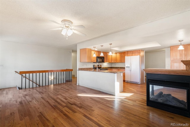 kitchen featuring light wood finished floors, white refrigerator with ice dispenser, black microwave, and a textured ceiling