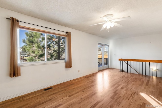 unfurnished room featuring visible vents, ceiling fan, a textured ceiling, wood finished floors, and baseboards