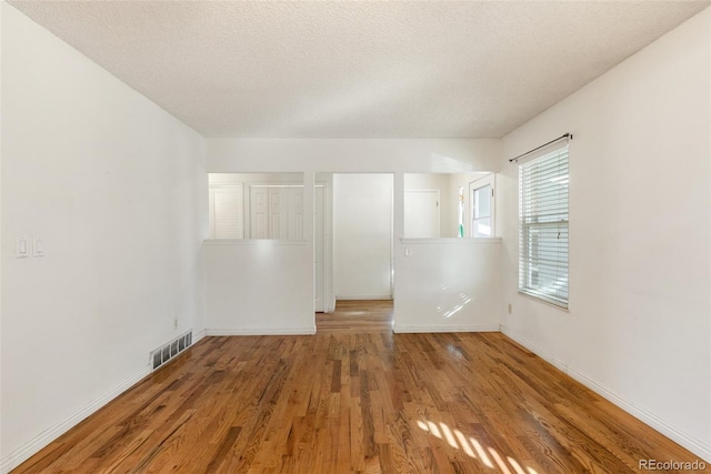 unfurnished room with baseboards, a textured ceiling, visible vents, and wood finished floors