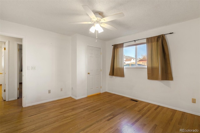 empty room with baseboards, visible vents, a ceiling fan, wood finished floors, and a textured ceiling