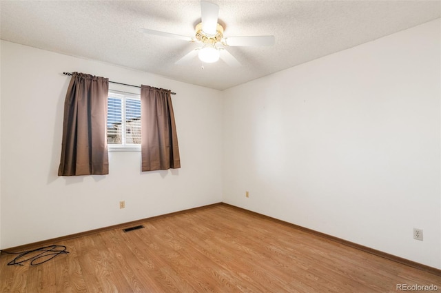 spare room featuring light wood finished floors, a ceiling fan, visible vents, and a textured ceiling