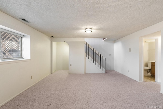 basement with a textured ceiling, stairs, visible vents, and carpet flooring