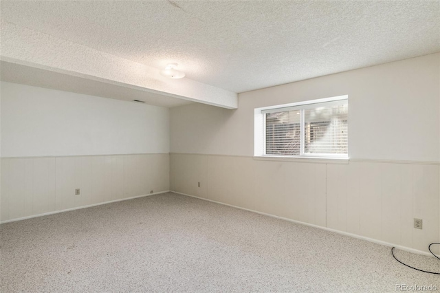 carpeted empty room featuring a textured ceiling and wainscoting