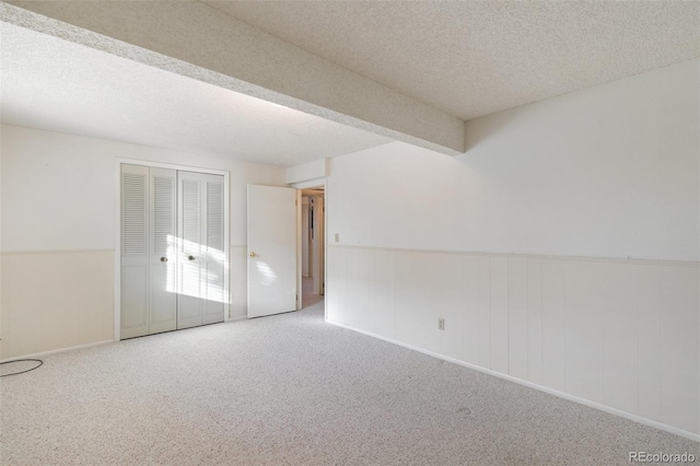 empty room featuring a wainscoted wall, carpet flooring, beamed ceiling, and a textured ceiling