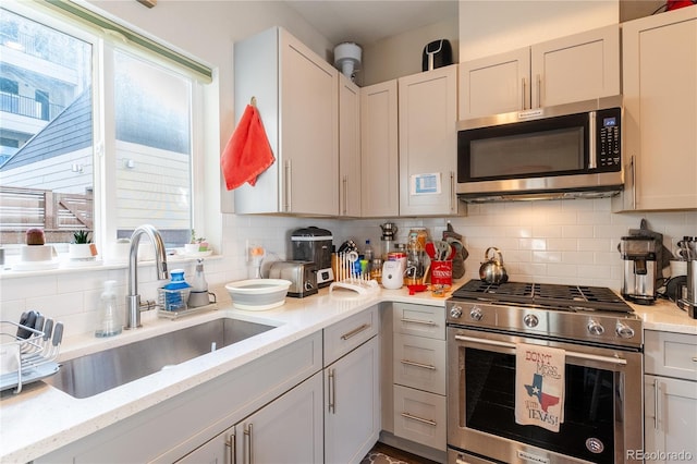 kitchen with stainless steel appliances, light stone countertops, sink, white cabinets, and decorative backsplash