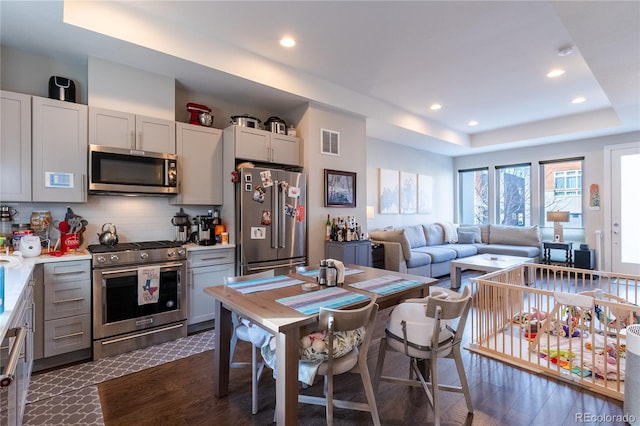 kitchen with appliances with stainless steel finishes, gray cabinetry, backsplash, a tray ceiling, and dark hardwood / wood-style floors