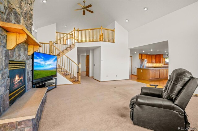 living room featuring ceiling fan, a fireplace, high vaulted ceiling, and light carpet