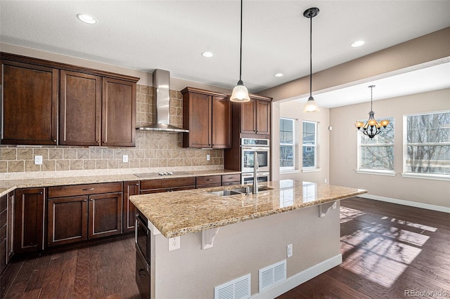 kitchen with wall chimney exhaust hood, dark hardwood / wood-style flooring, light stone countertops, and a breakfast bar