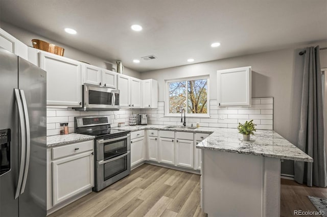 kitchen with sink, white cabinetry, light hardwood / wood-style flooring, appliances with stainless steel finishes, and light stone countertops