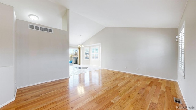 unfurnished living room featuring a notable chandelier, light wood-type flooring, and vaulted ceiling