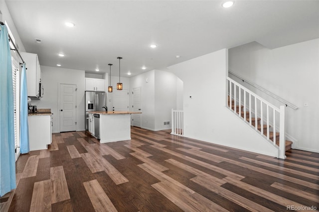 kitchen with pendant lighting, a center island with sink, white cabinetry, stainless steel appliances, and dark hardwood / wood-style flooring