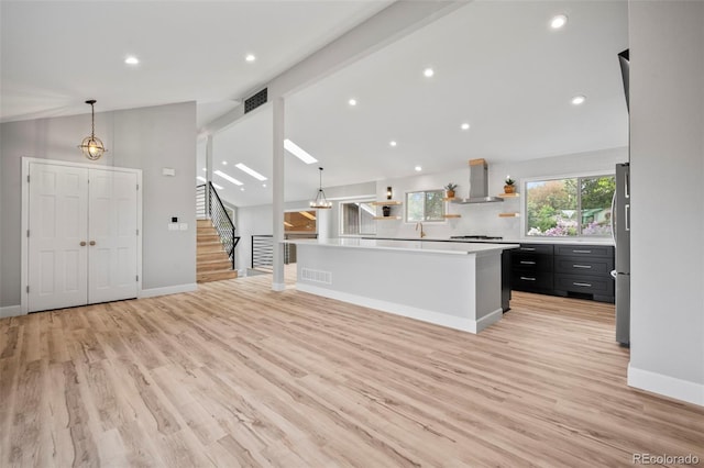 kitchen with lofted ceiling, wall chimney exhaust hood, decorative light fixtures, light hardwood / wood-style floors, and stainless steel fridge