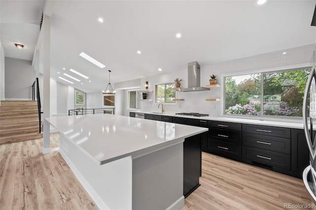 kitchen featuring appliances with stainless steel finishes, wall chimney exhaust hood, light hardwood / wood-style flooring, and a spacious island