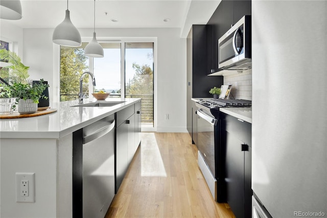 kitchen with appliances with stainless steel finishes, decorative light fixtures, sink, backsplash, and light wood-type flooring