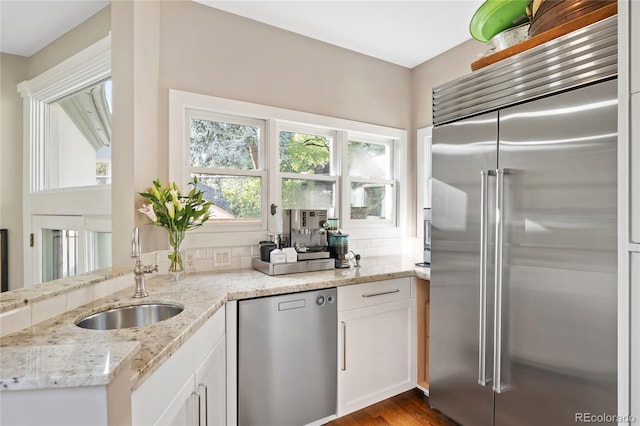 kitchen featuring hardwood / wood-style flooring, stainless steel appliances, sink, white cabinetry, and light stone counters