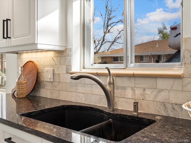 kitchen with white cabinets, decorative backsplash, dark stone counters, and sink