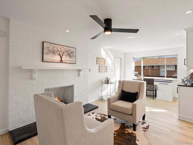 living room with ceiling fan, light hardwood / wood-style flooring, and a brick fireplace