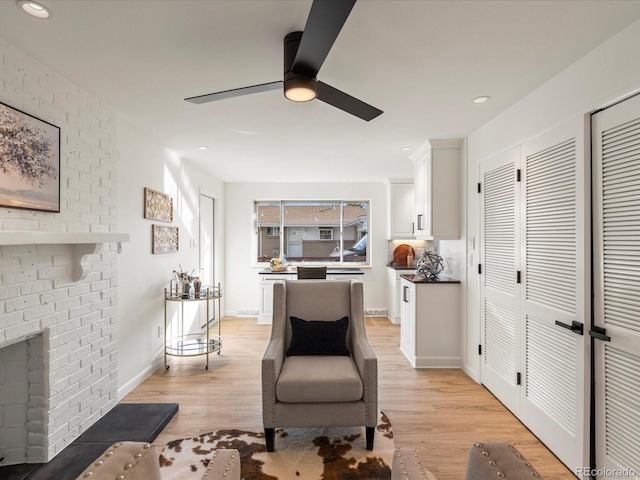 living room with ceiling fan, light hardwood / wood-style flooring, and a brick fireplace