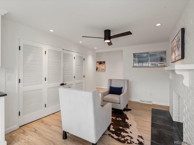 sitting room with ceiling fan, a fireplace, and light hardwood / wood-style flooring