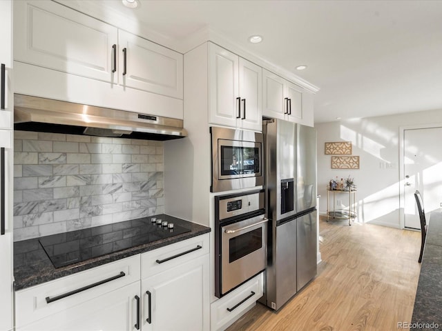 kitchen featuring range hood, light hardwood / wood-style floors, decorative backsplash, white cabinets, and appliances with stainless steel finishes