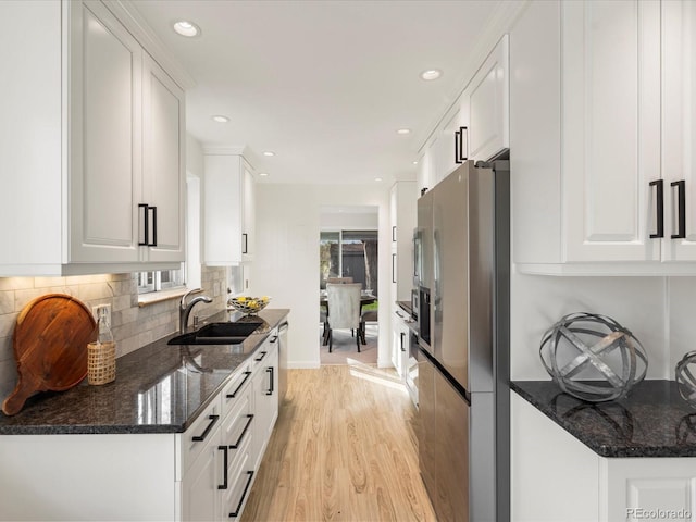 kitchen with dark stone counters, sink, light hardwood / wood-style floors, white cabinetry, and stainless steel refrigerator