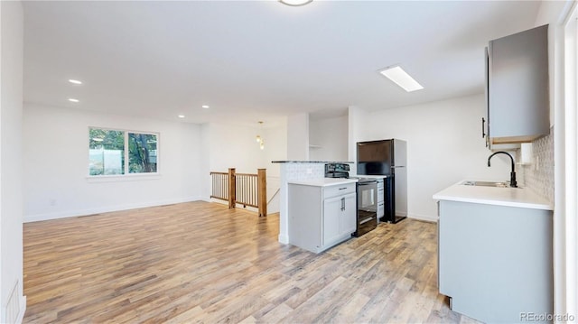 kitchen with a sink, light countertops, black appliances, light wood finished floors, and tasteful backsplash