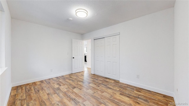 unfurnished bedroom with a closet, a textured ceiling, baseboards, and wood finished floors